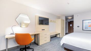 A hotel room with a bed, desk, chair, wardrobe, and a mirror.