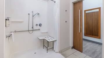 A modern bathroom with a shower, a small table, and a wooden door.