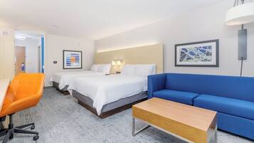 Quarto de hotel com cama, sofá azul, mesa de madeira, cadeira laranja e luminária fixada na parede.