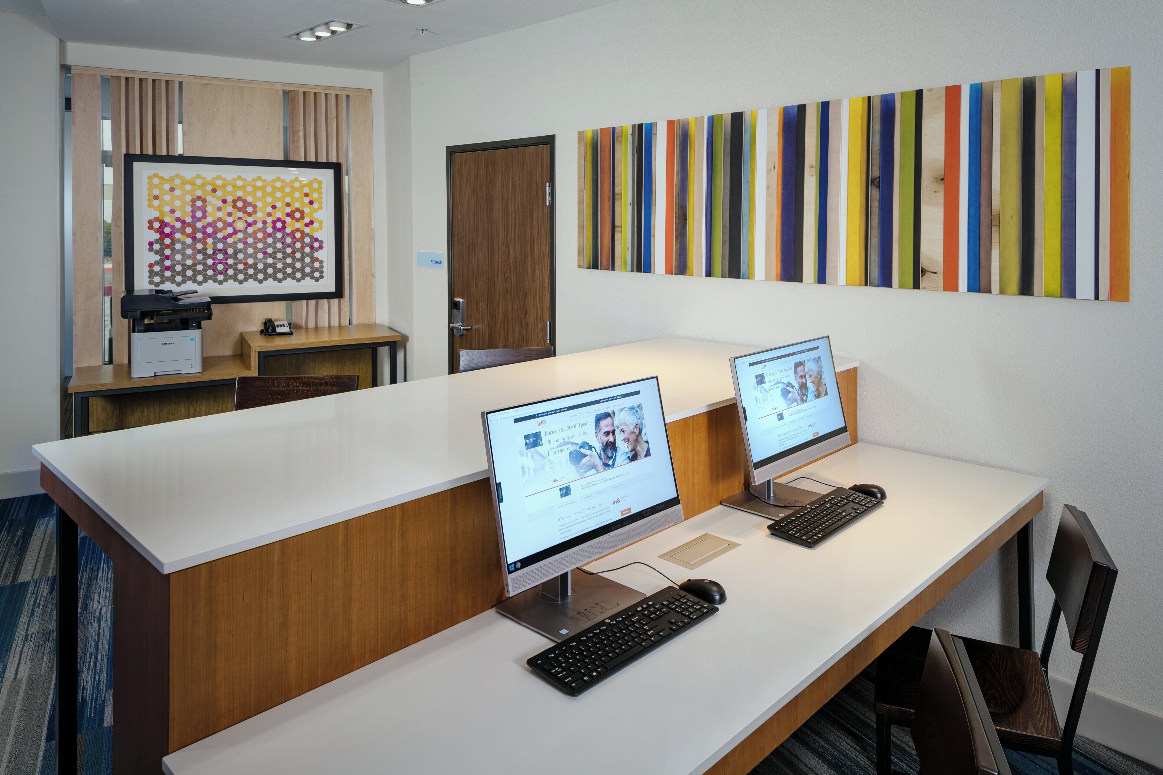 Een moderne kantoorruimte met twee bureaus, elk met een computer en toetsenbord, en een groot abstract schilderij aan de muur.