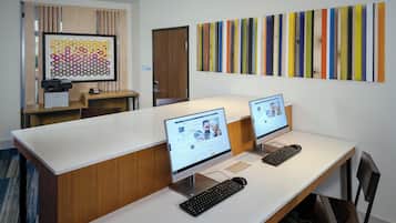 Een moderne kantoorruimte met twee bureaus, elk met een computer en toetsenbord, en een groot abstract schilderij aan de muur.