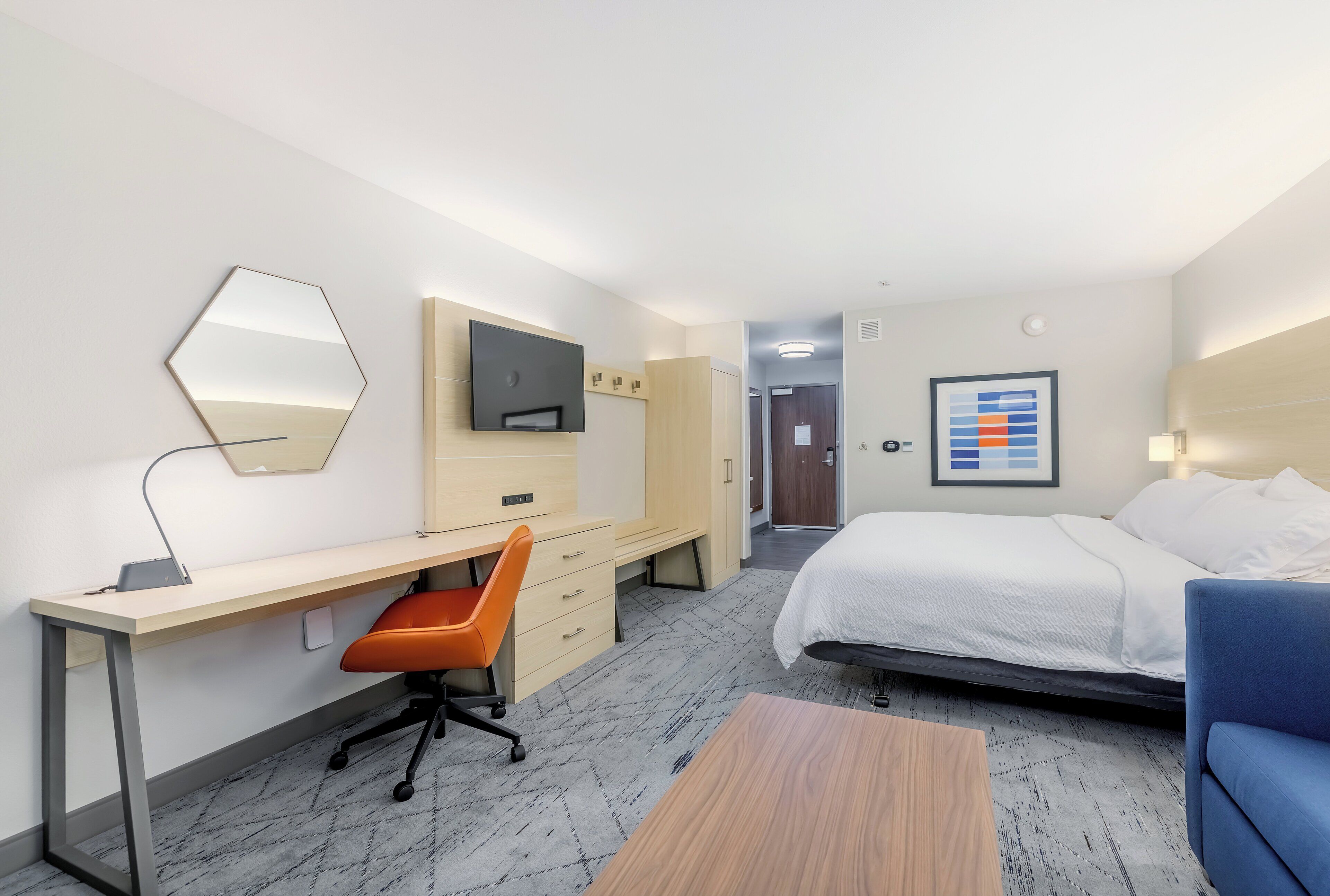 A hotel room with a bed, desk, chair, and a TV.