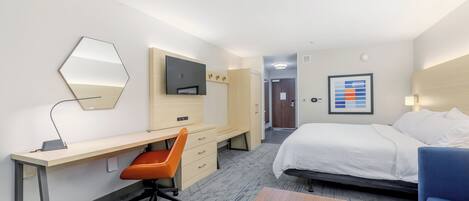 A hotel room with a bed, desk, chair, and a TV.