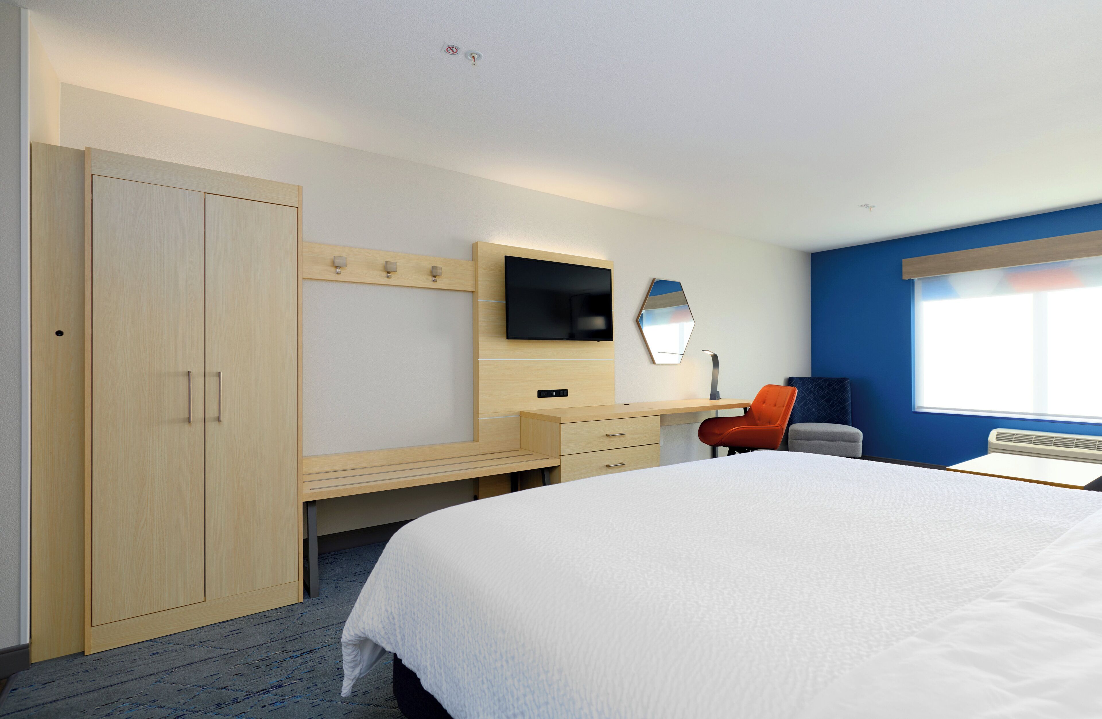 A hotel room with a bed, a desk, a TV, a wardrobe, and a window.