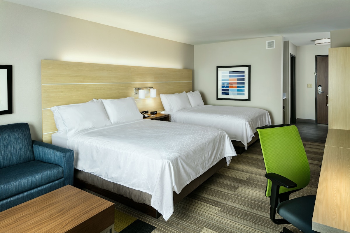 A hotel room with two beds, a desk, a chair, a sofa, and a framed picture on the wall.