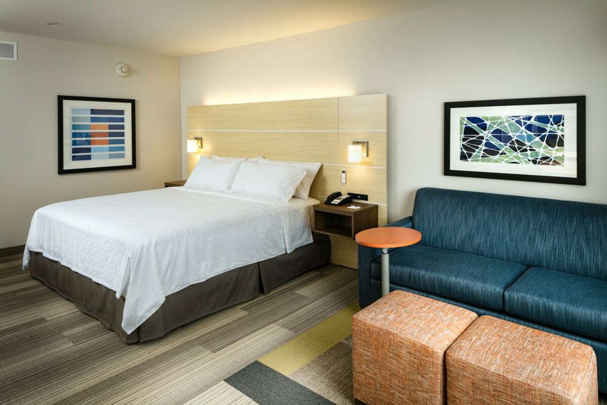 A hotel room with a bed, a blue sofa, a small round table, and two framed pictures on the wall.
