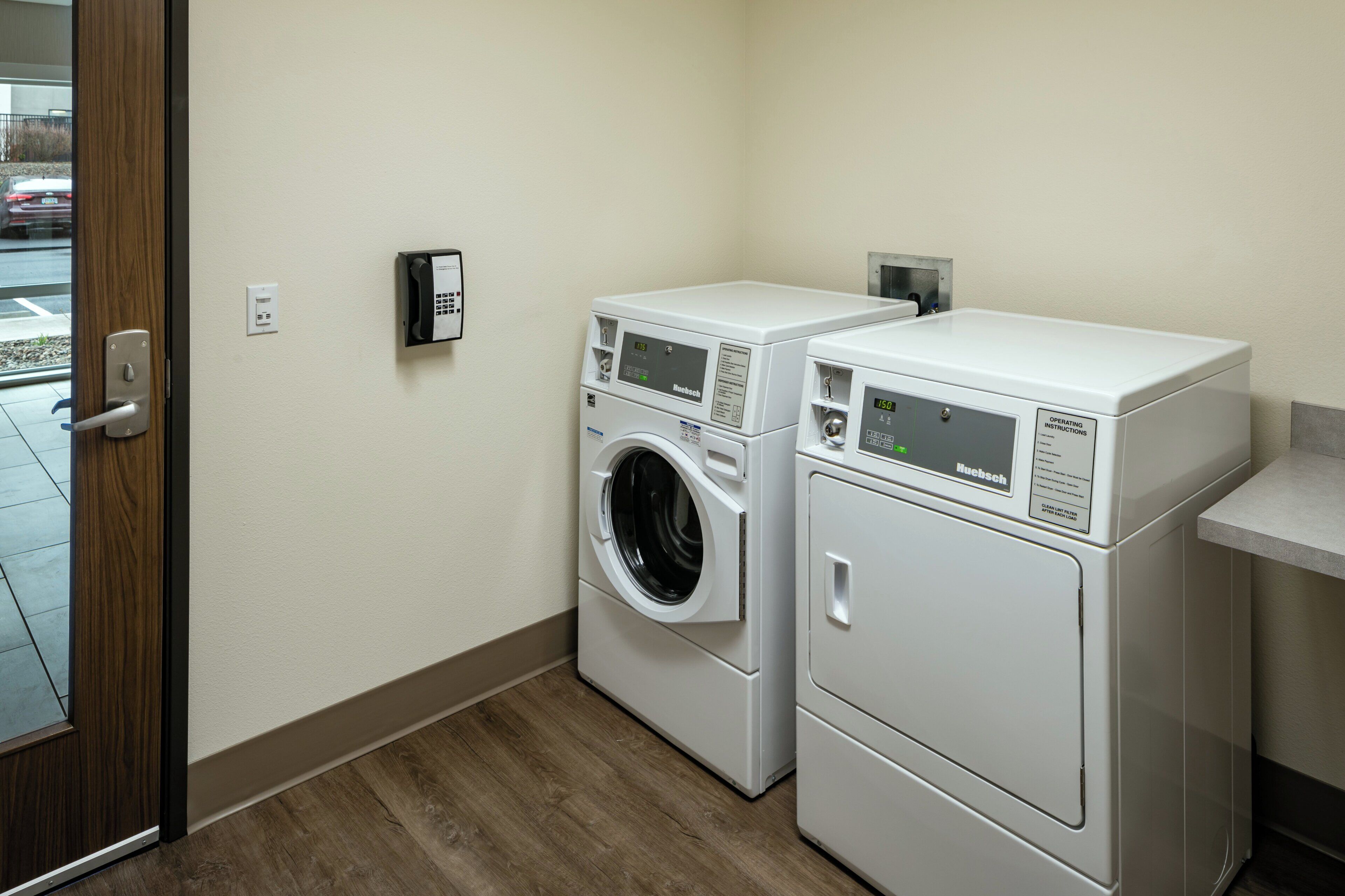 A laundry room with two front-loading washing machines and a control panel on the wall.