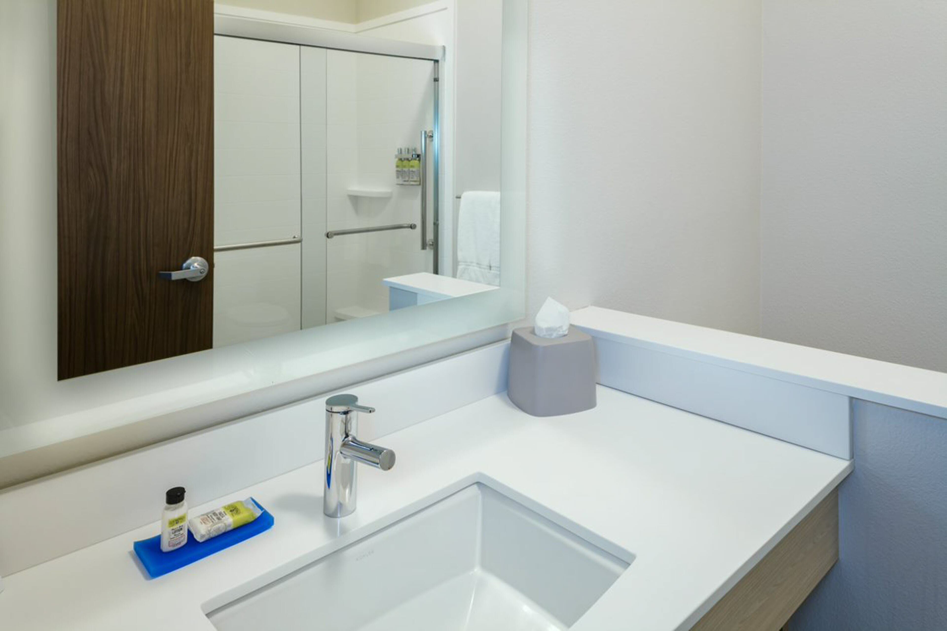 A modern bathroom with a white sink, a mirror, a towel rack, and a wooden door.