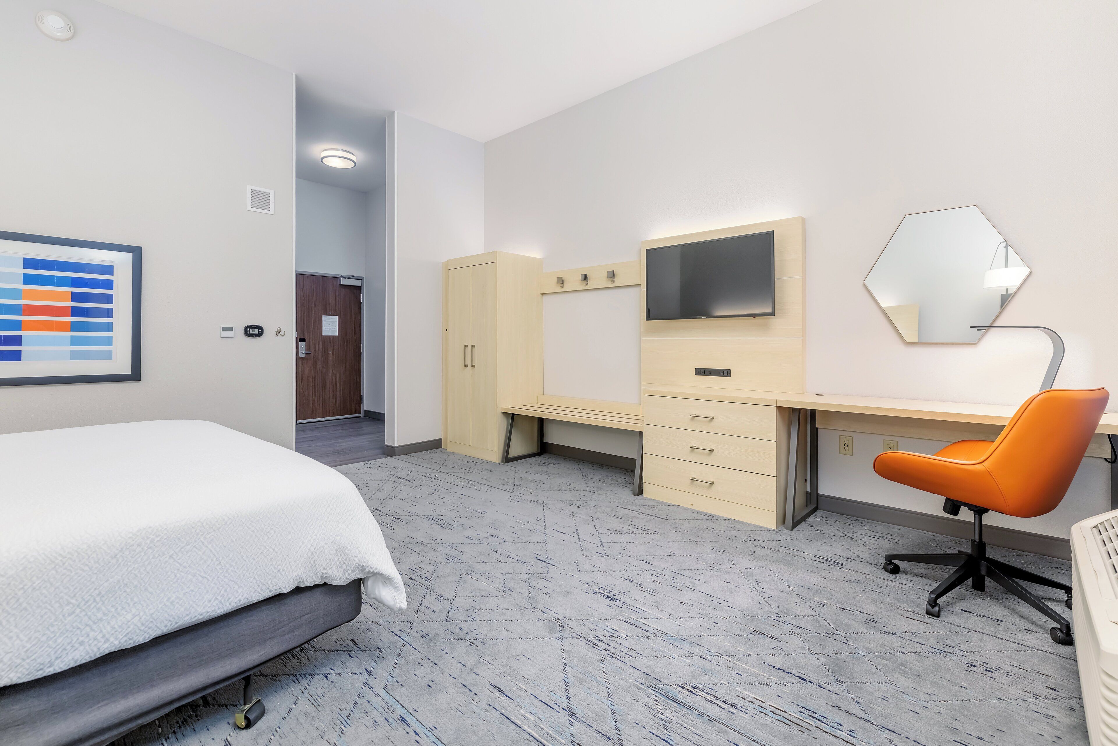 Una habitación de hotel con cama, escritorio, silla, televisión, espejo y puerta.