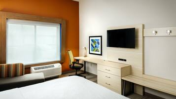 Een hotelkamer met een groot bed, een bureau met stoel, een televisie en een raam met zonwering.