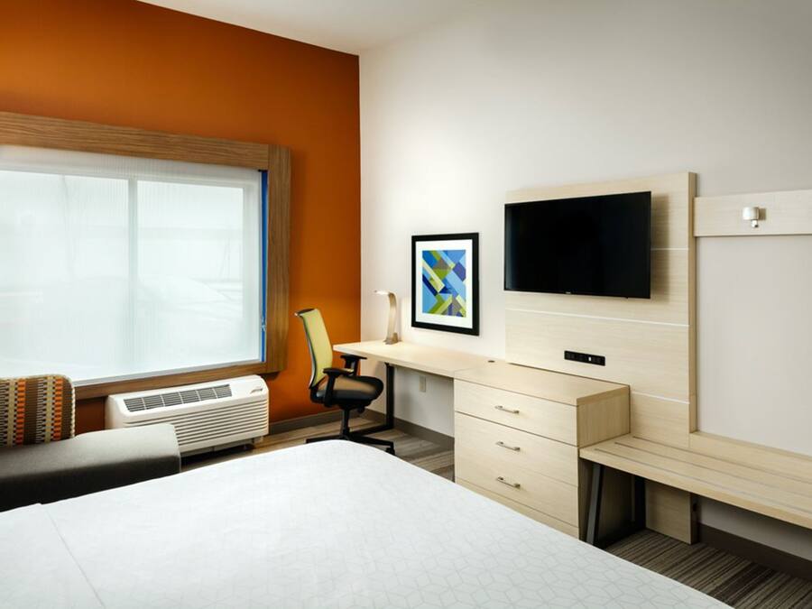 Een hotelkamer met een groot bed, een bureau met stoel, een televisie en een raam met zonwering.