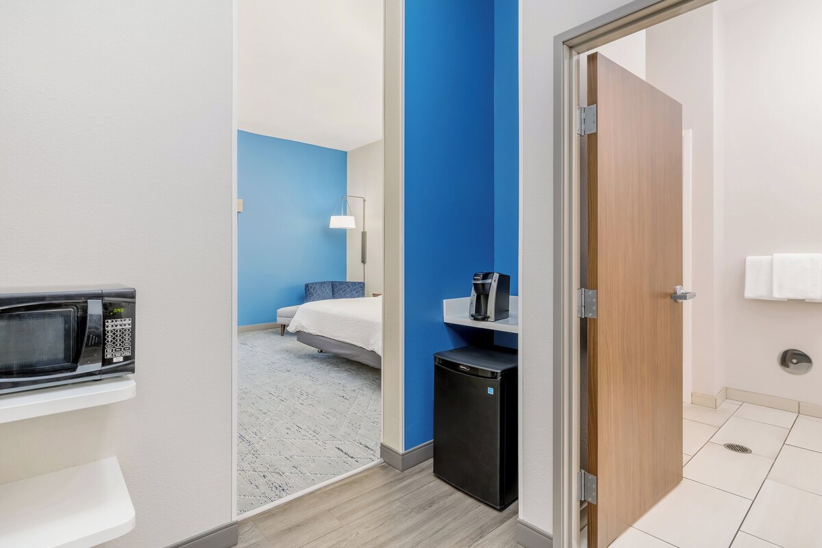 A hotel room with a microwave, a small refrigerator, a bed, and a bathroom with a toilet and sink.