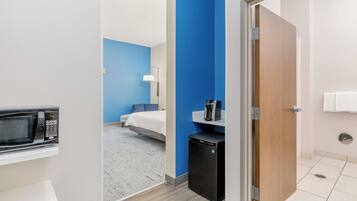 A hotel room with a microwave, a small refrigerator, a bed, and a bathroom with a toilet and sink.