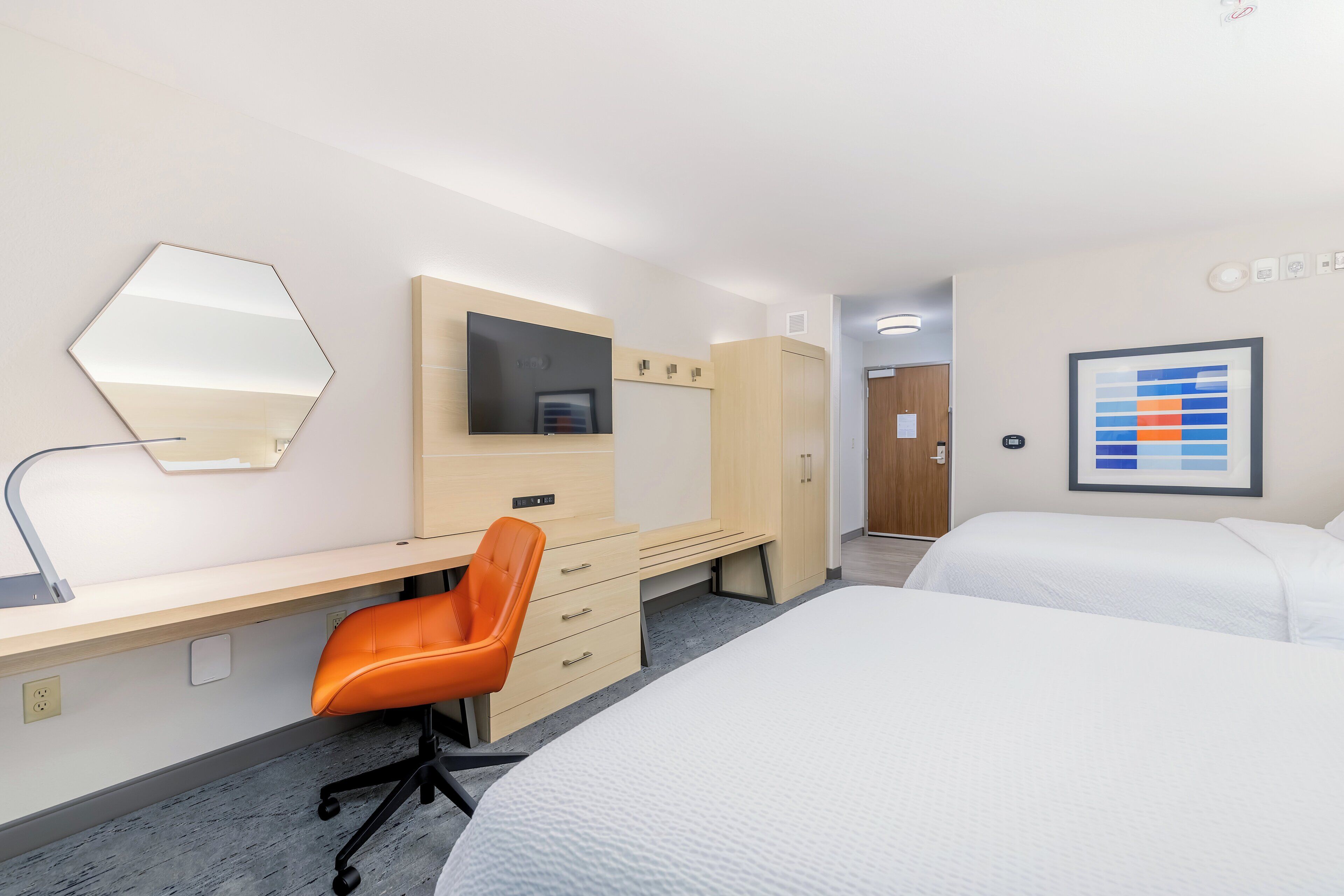 A hotel room with a desk, chair, bed, and a large mirror.