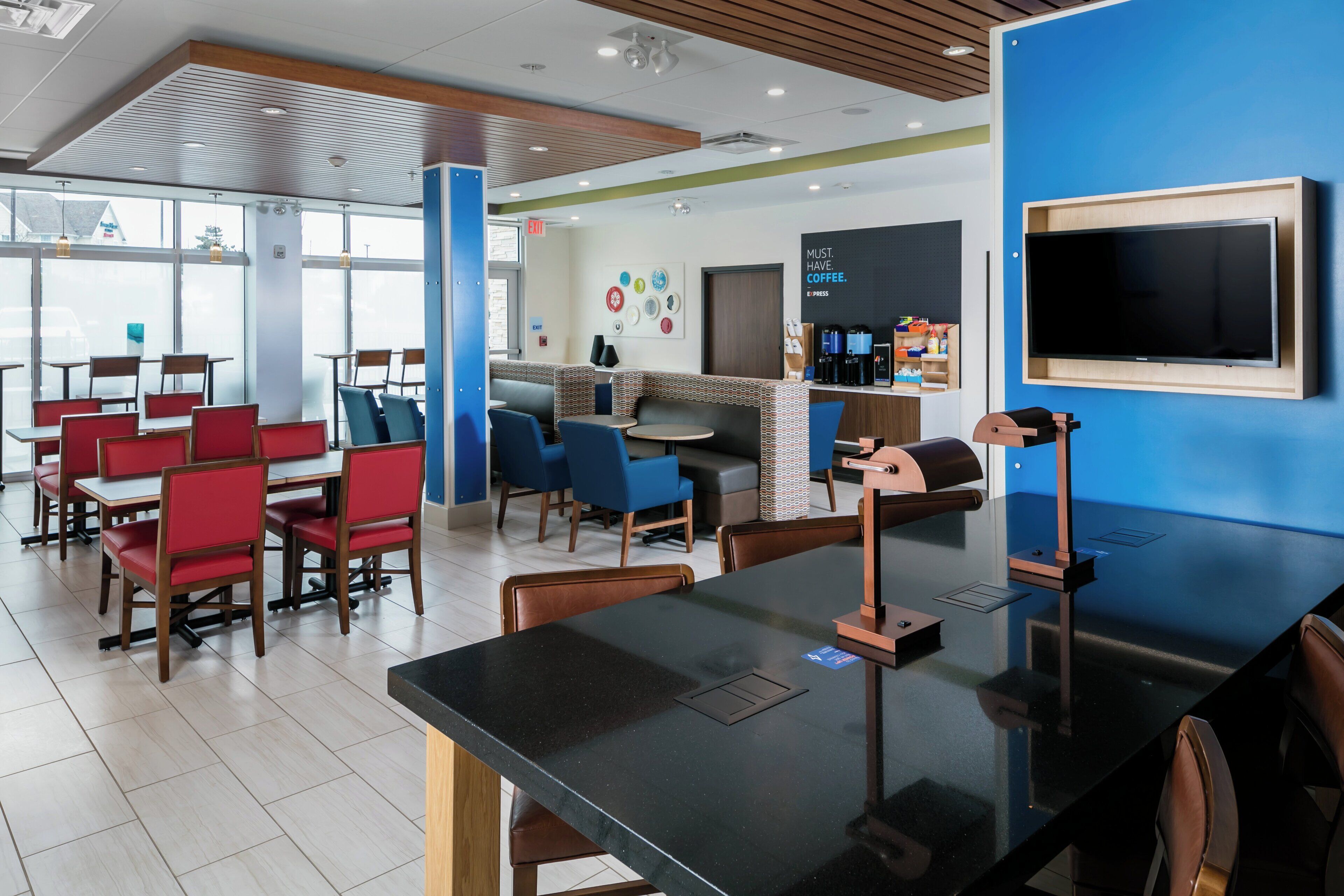Een moderne café met tafels, stoelen, een koffiehoek en een groot televisiescherm.