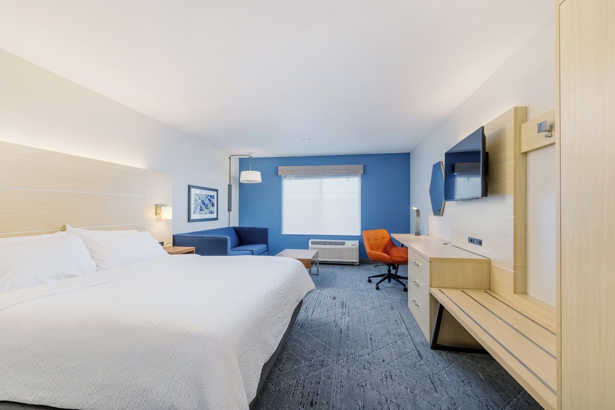 A hotel room with a bed, a desk, a chair, a TV, and a window.