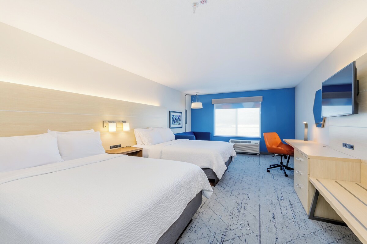 A hotel room with two beds, a desk, a chair, a TV, and a window.