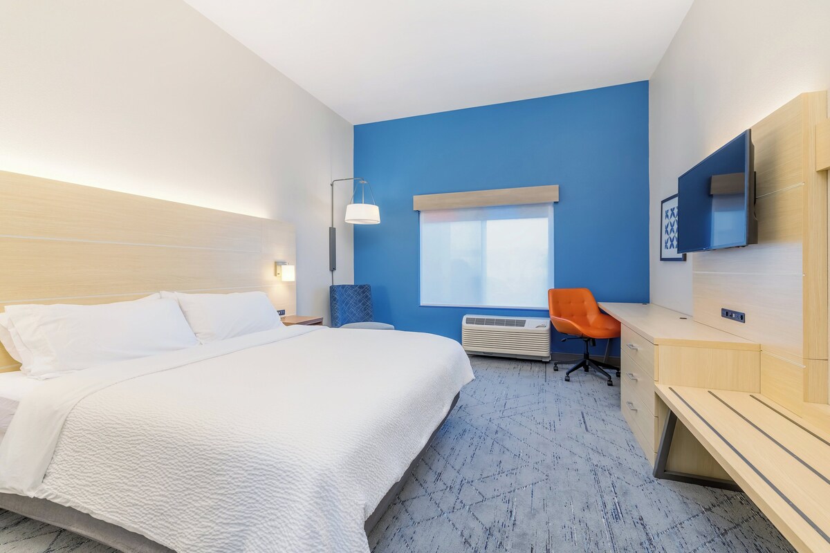 A hotel room with a bed, desk, chair, and a large window.
