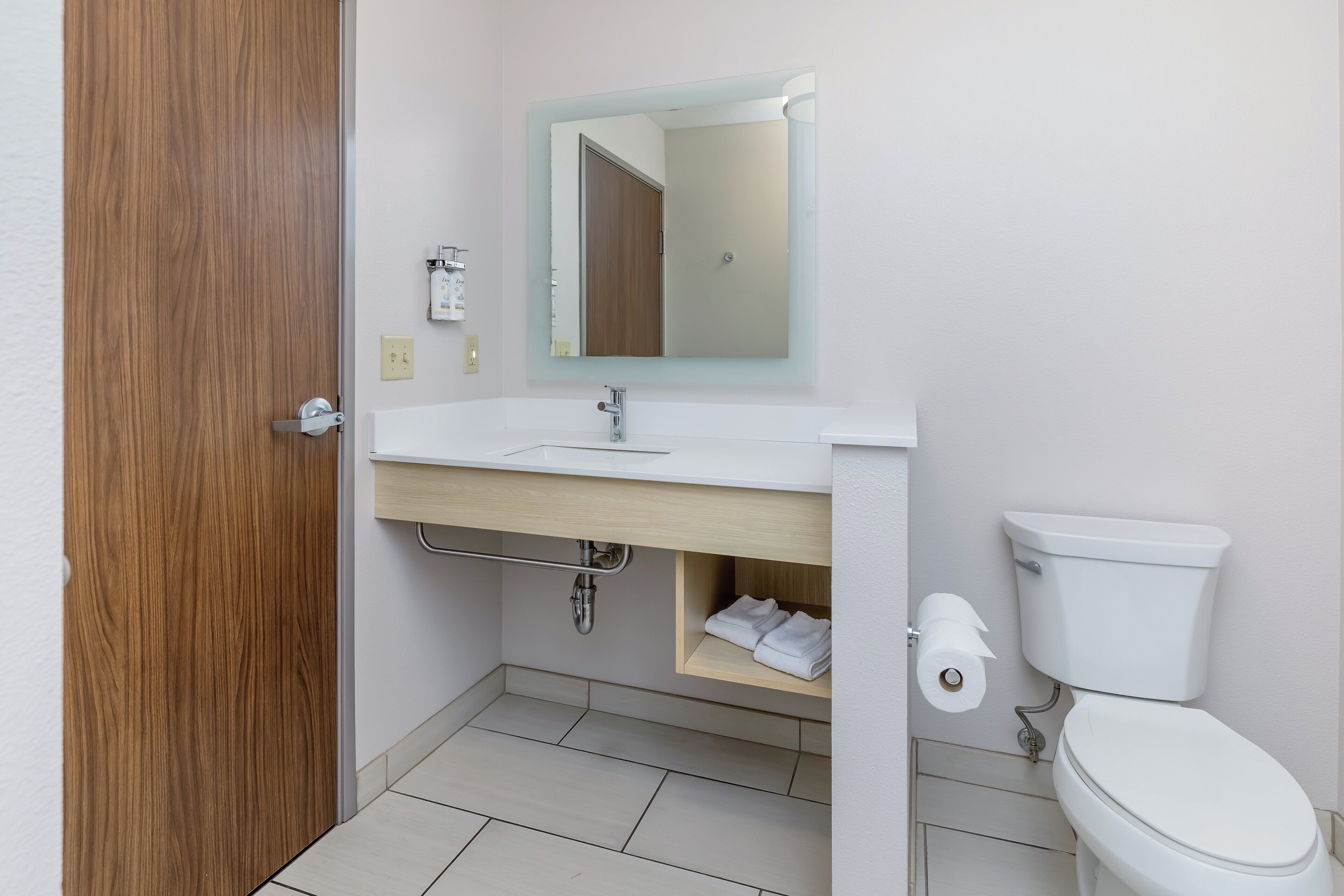 A bathroom with a wooden door, a white sink with a mirror, a toilet, and a towel rack.