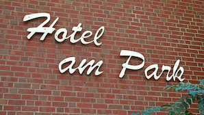 Een hotelschild met de naam 'Hotel am Park' op een rode bakstenen muur.