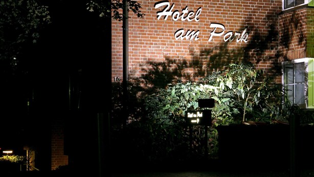 Een gebouw van baksteen met een bord waarop staat: Hotel am Park, 's nachts.