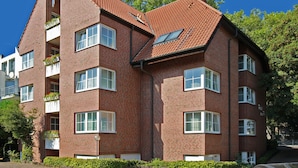 Een hotel van rode baksteen met veel ramen en balkons, met een schuin dak en een heldere blauwe lucht op de achtergrond.