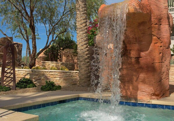 A pool with a waterfall feature, surrounded by rock formations and greenery.