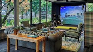 A modern living room with a large TV displaying a golf game, comfortable seating, and a view of the outdoors. - Graduate by Hilton Eugene (Eugene)
