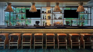 A bar area with multiple wooden stools, a counter with bottles and glasses, and hanging wicker lamps. - Graduate by Hilton Eugene (Eugene)