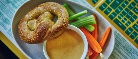 Prato com pretzel, aipo, cenouras e uma tigela de molho sobre uma mesa com um menu.