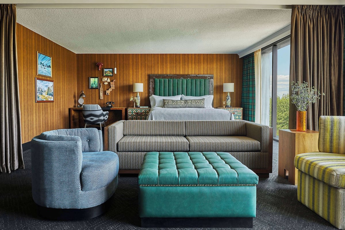 A hotel room with a bed, a sofa, an ottoman, and two armchairs.