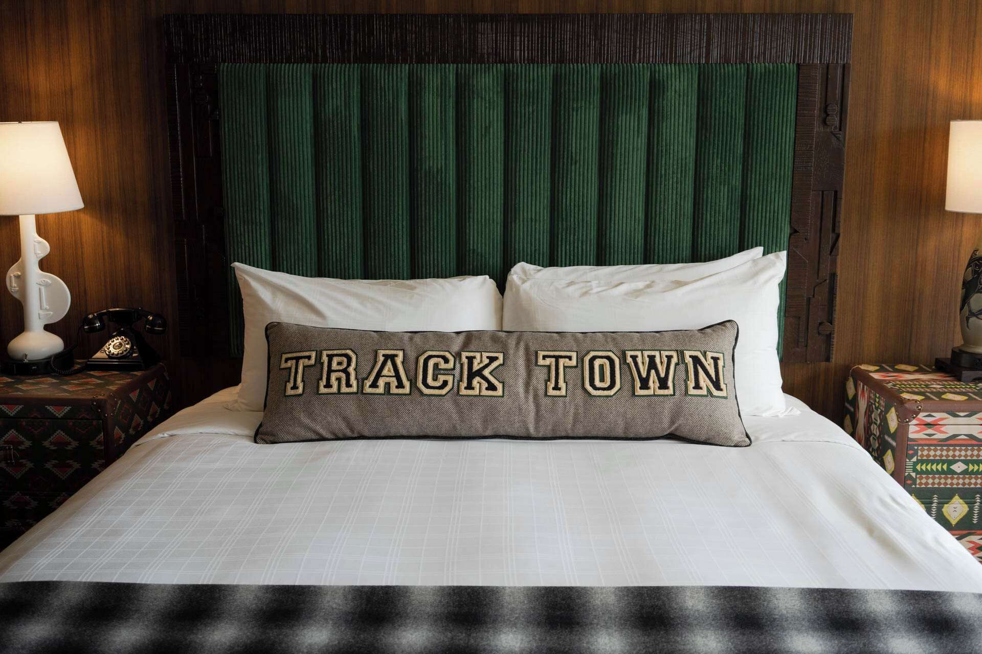 Ein Bett mit einem Kopfkissen, das den Schriftzug "TRACK TOWN" zeigt, und einem grünen Kopfteil.
