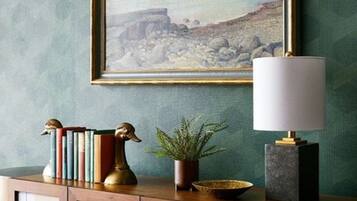 A wooden cabinet with a framed landscape painting above it, a lamp, and decorative items including books and a plant.