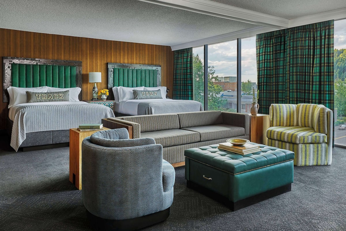 A hotel room with two beds, a sofa, a chair, and a view of a cityscape.