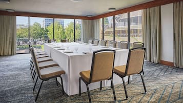 A conference room with a long table, chairs, and large windows offering a city view.