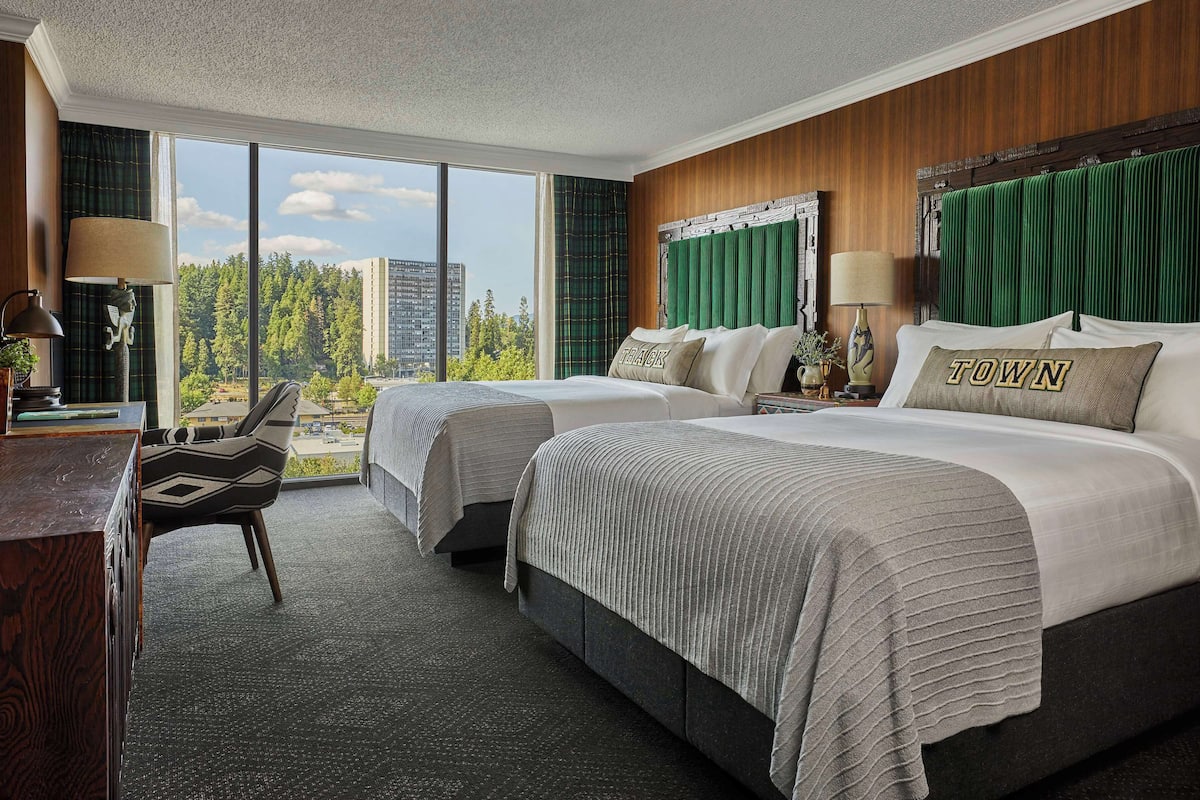 A hotel room with two beds, a desk, and a view of the city.