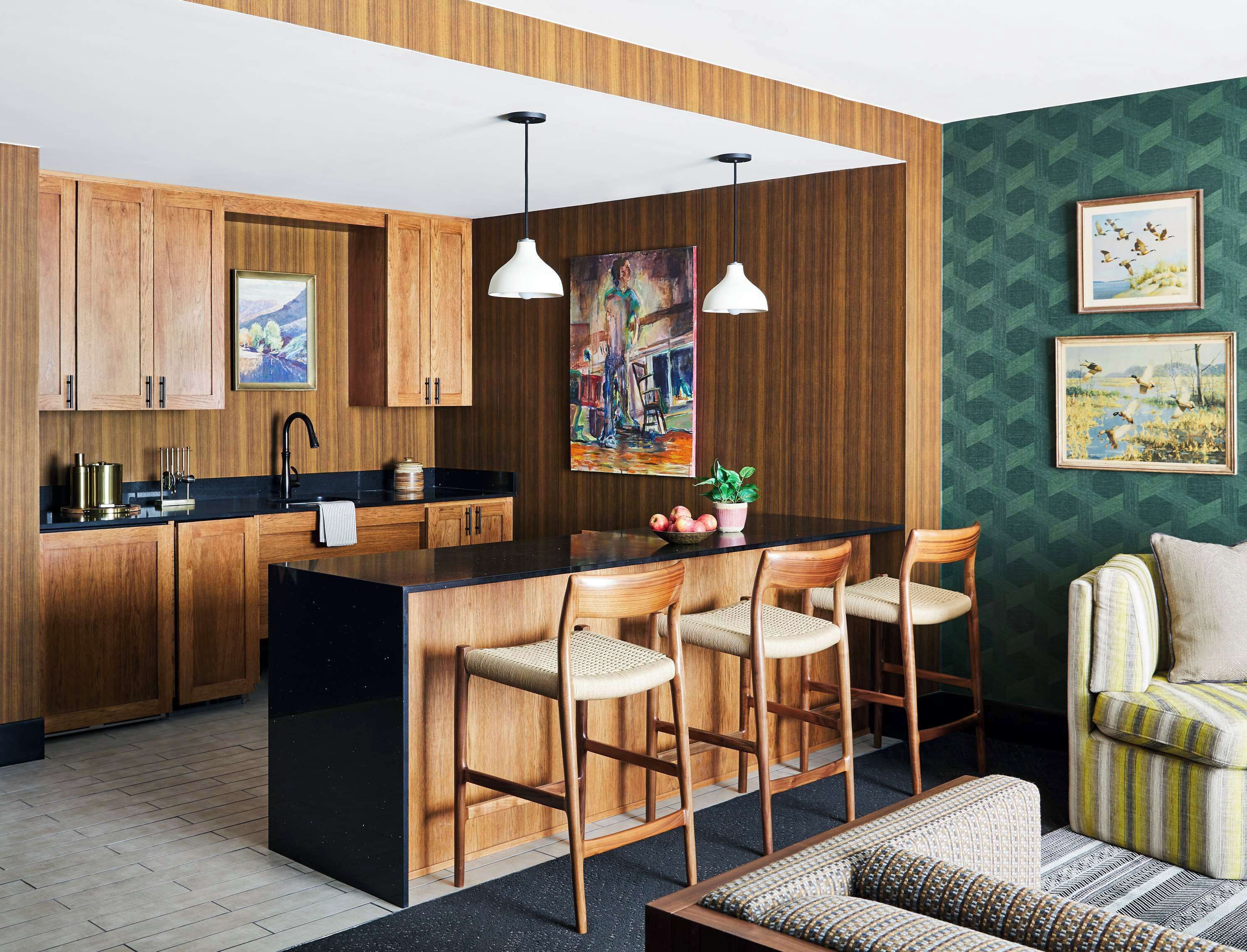 Cocina moderna con armarios de madera, encimera negra y una isla central con taburetes de bar. Hay un cuadro en la pared y una foto enmarcada sobre la isla.
