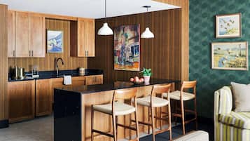 Cocina moderna con armarios de madera, encimera negra y una isla central con taburetes de bar. Hay un cuadro en la pared y una foto enmarcada sobre la isla.