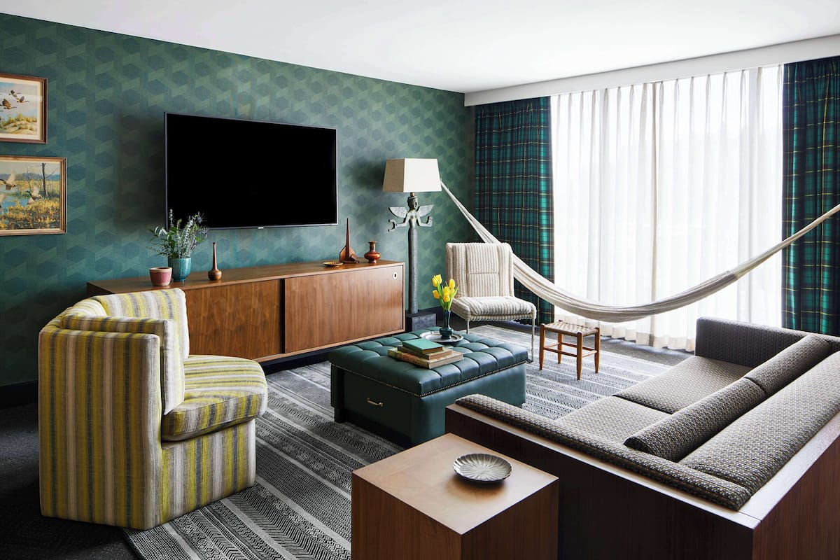 A living room with a sofa, armchair, ottoman, and a flat-screen TV mounted on the wall.