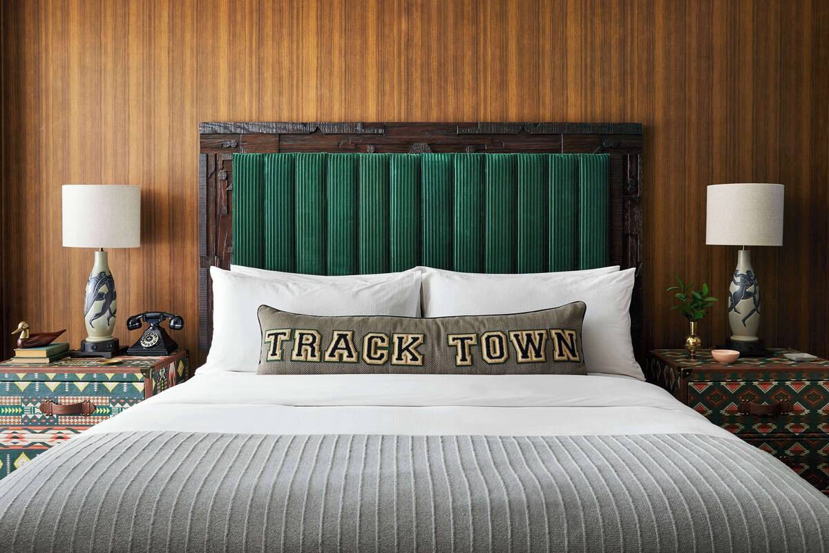 A bed with a green headboard, two bedside tables with lamps, and a pillow with "TRACK TOWN" text.