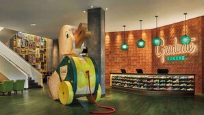 A lobby with a large wooden sculpture, a staircase, a wall of framed pictures, and a shoe display. - Graduate by Hilton Eugene (Eugene)