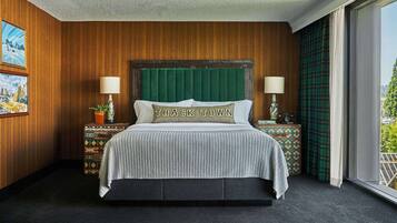 A hotel room with a wooden paneled wall, a bed with a green headboard, two bedside lamps, and a window with a view of greenery.