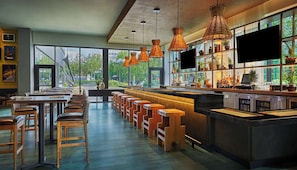 Un bar moderno con taburetes altos, una barra larga e iluminación colgante.