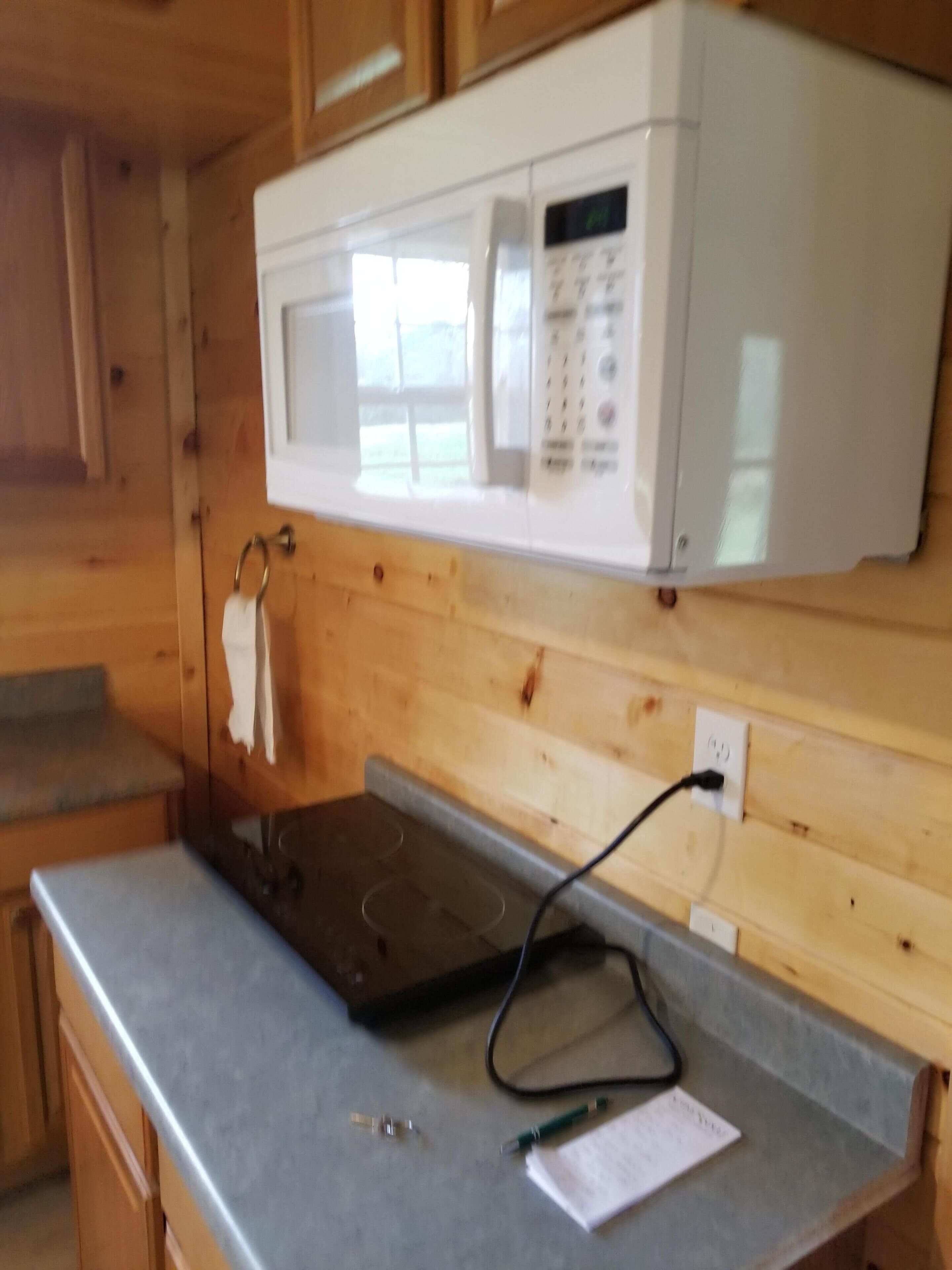 A kitchen with wooden cabinets, a microwave, a countertop, and a kettle.