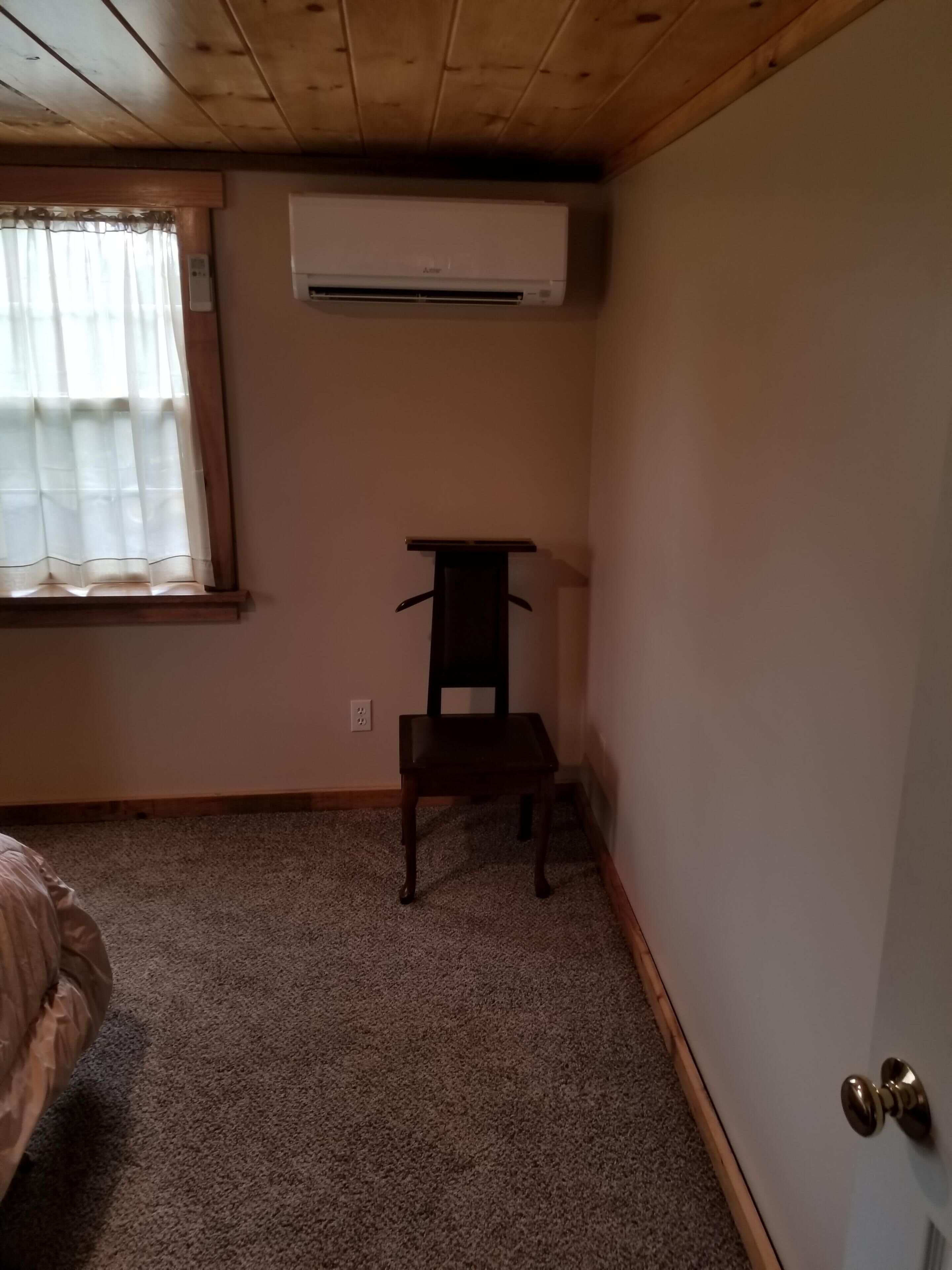 Een kamer met een houten plafond, een wandunit voor airconditioning, een stoel en een deur met een messing knop.