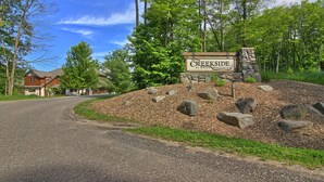 A sign for Creekside at Boyne Mountain, surrounded by a gravel road and a landscaped area with rocks and trees. - Jump onto the Disciples 8 Chairlift - 7317 Creekside Condo, Ski in/Ski out (Boyne City)