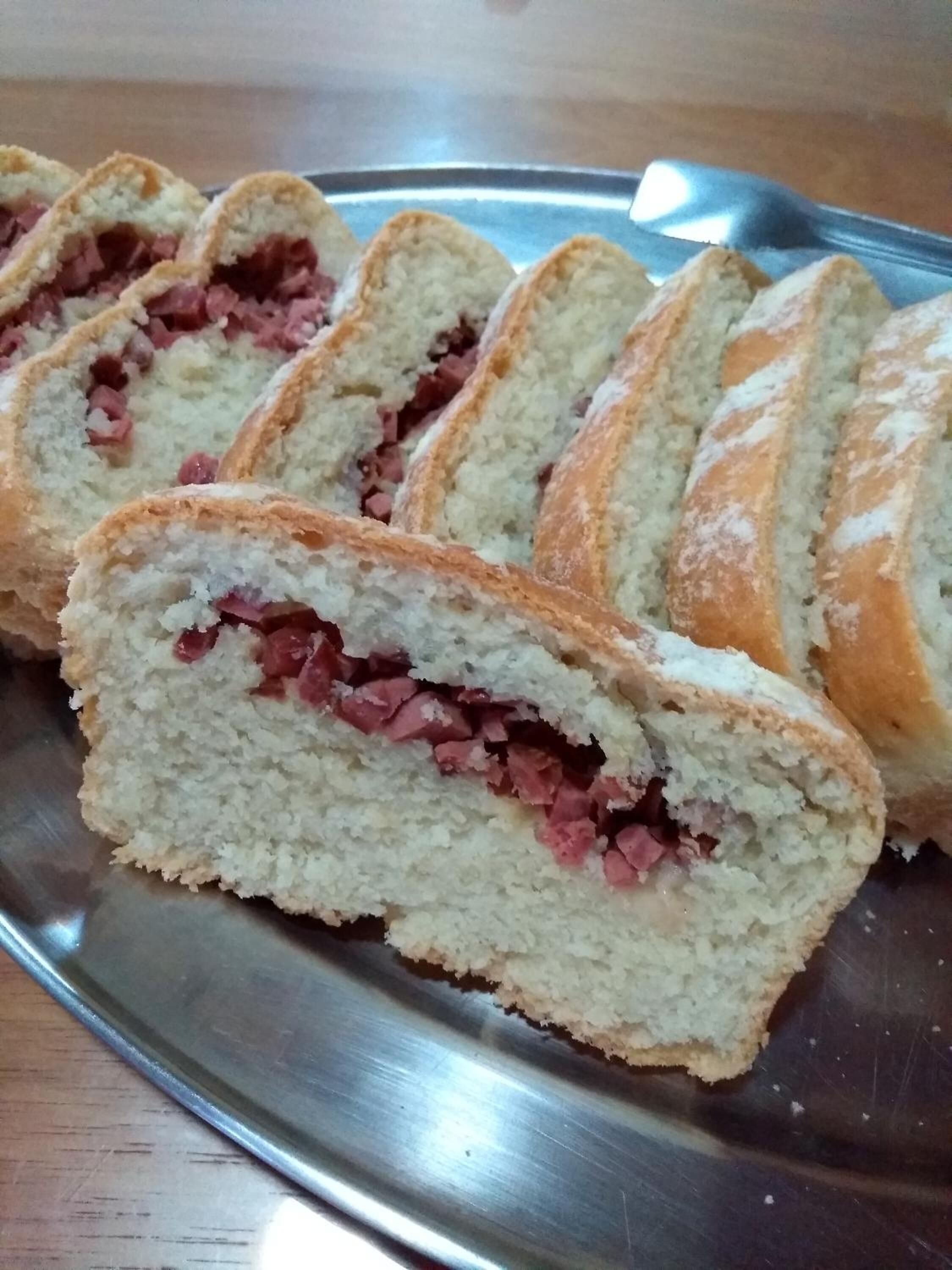 Uma bandeja de metal com pães de forma fatiados e recheio rosado.