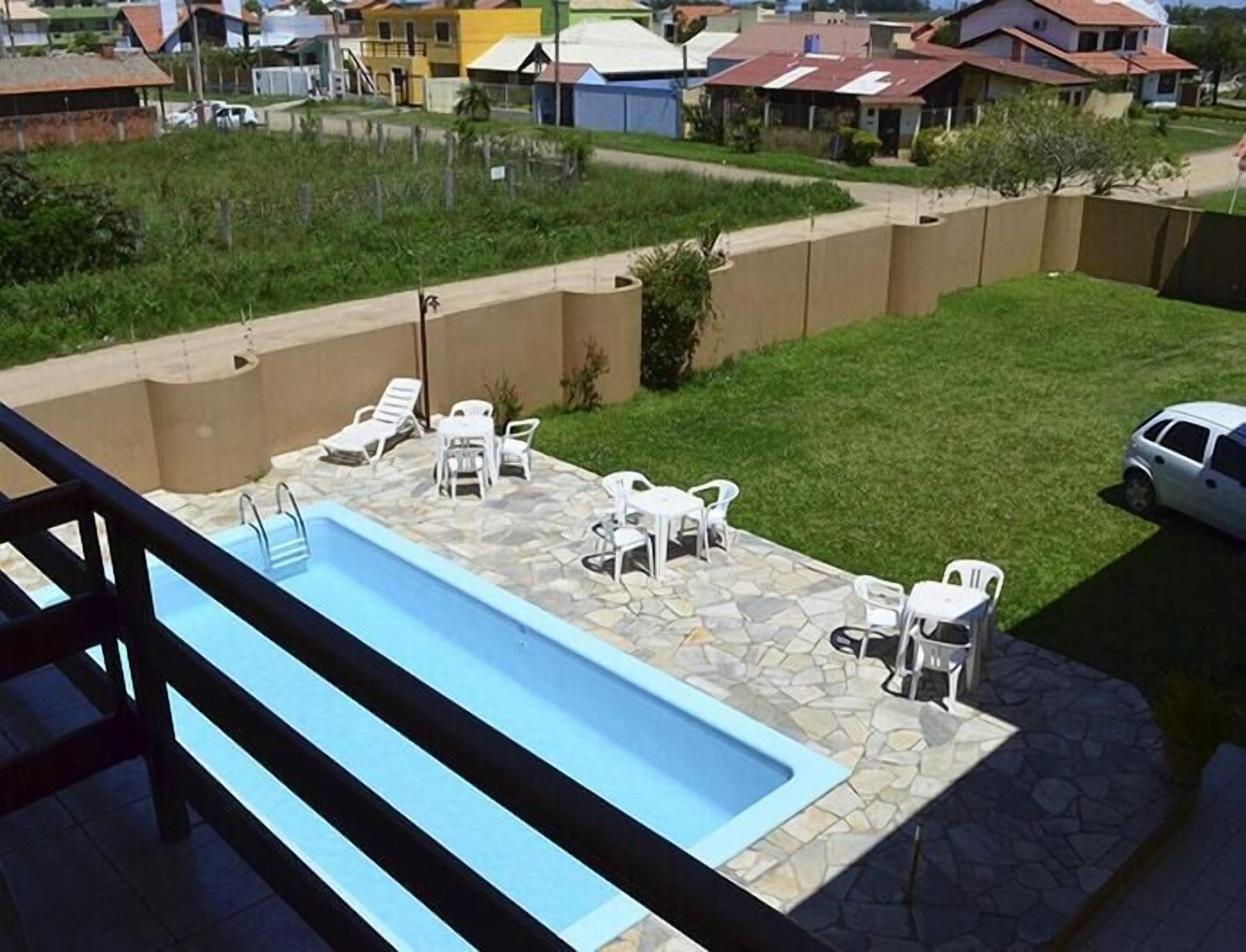 A swimming pool with lounge chairs and a stone deck, surrounded by a low wall and a grassy area.