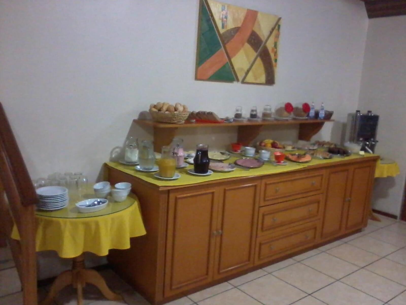 A dining area with a buffet setup, including a glass table, wooden cabinet, and various food items.