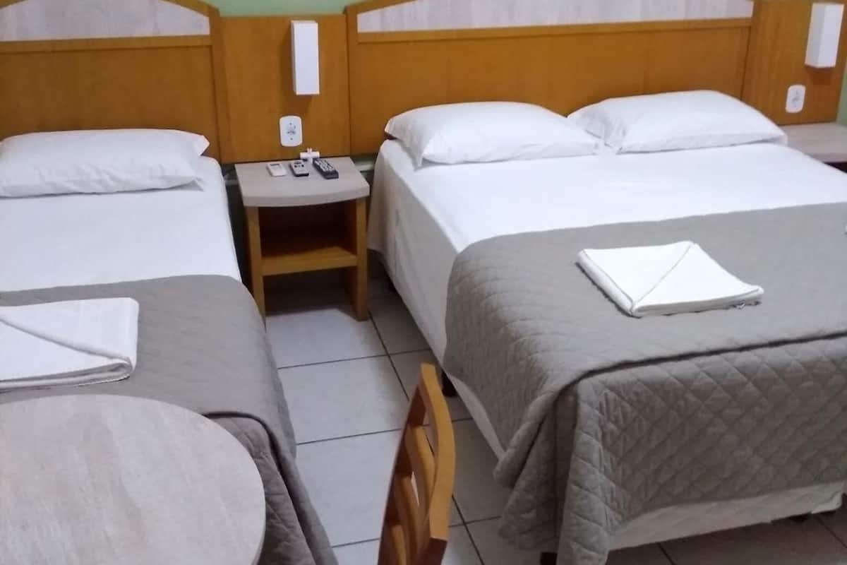 Habitación de hotel con dos camas, una mesita, una silla y una mesita de noche con teléfono y controles remotos.